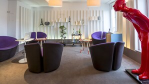 Ein modernes Interieur mit einem Schreibtisch, violetten Stühlen, einer roten Skulptur und einem Bücherregal.