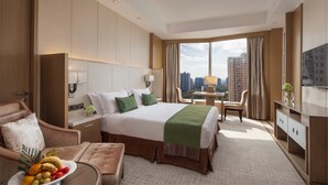 Habitación de hotel con una cama grande, un área de descanso con una mesa y sillas, una televisión y vistas a la ciudad.