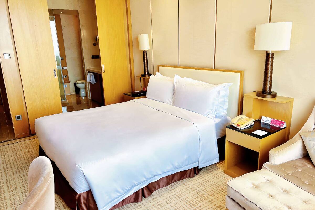 Une chambre d’hôtel avec un grand lit, une table de chevet avec une lampe, une chaise et une petite table avec un téléphone et une carte.