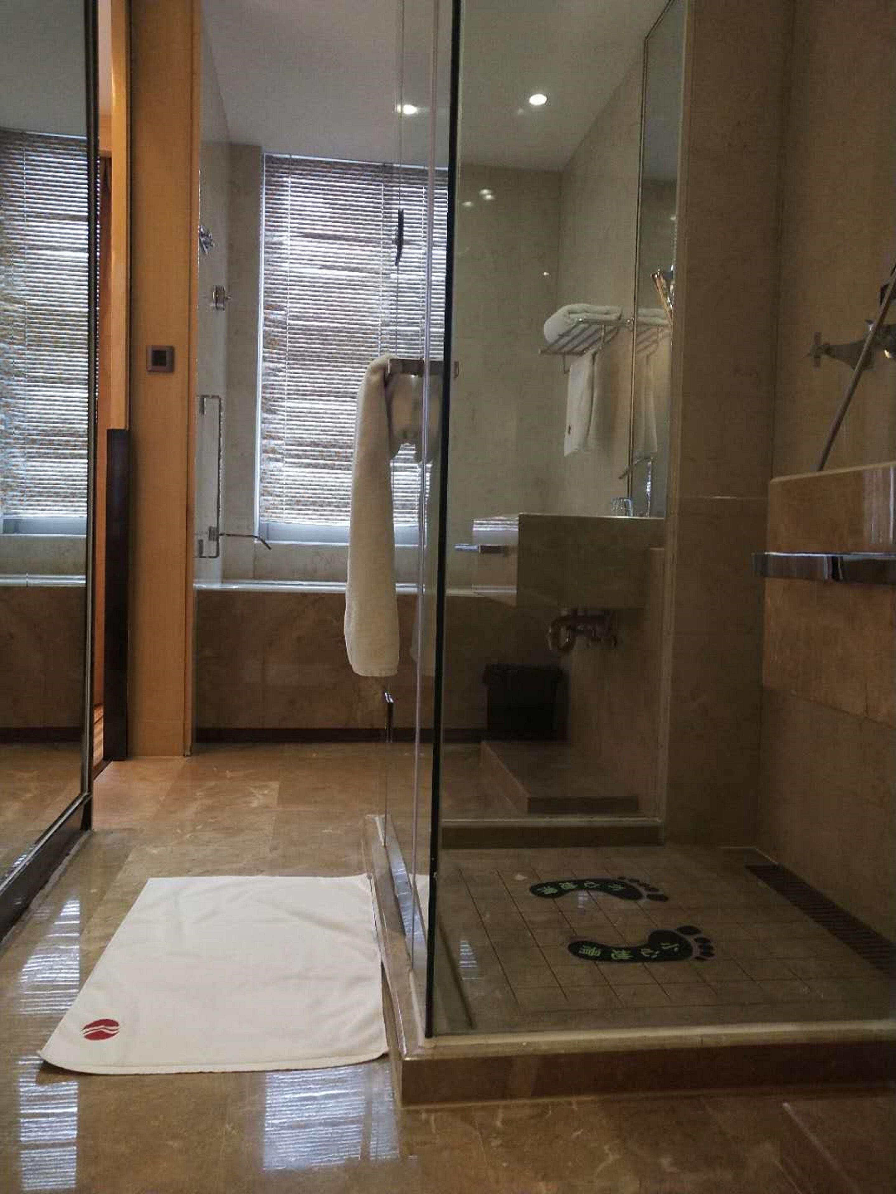 A modern bathroom with a glass shower enclosure, a white towel hanging on the wall, and a mat on the floor.