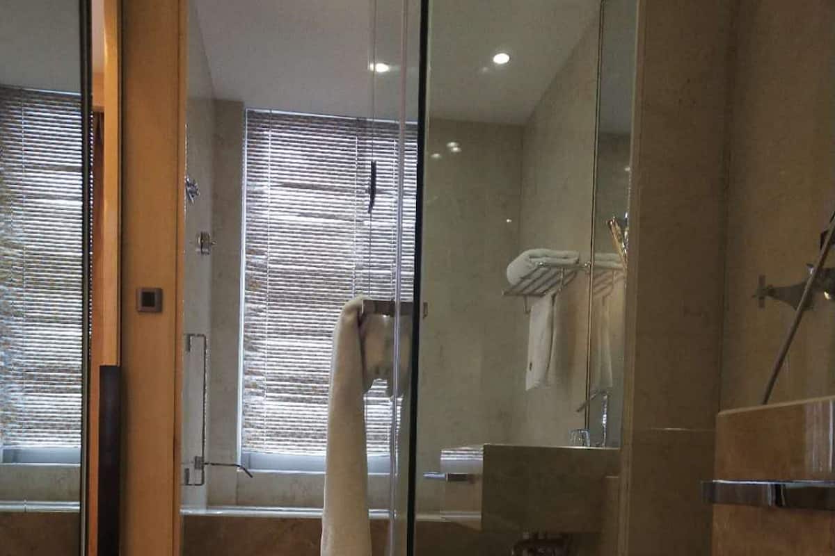 A modern bathroom with a glass shower enclosure, a white towel hanging on the wall, and a mat on the floor.