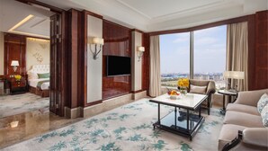 Habitación de hotel con un ventanal grande, un televisor de pantalla plana, un sofá, una mesita de centro y una cama con cabecera.
