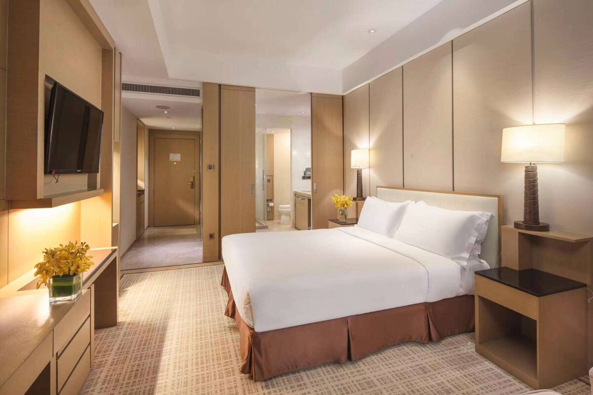Une chambre d’hôtel avec un grand lit, un téléviseur fixé au mur, une table de chevet avec une lampe et un miroir.