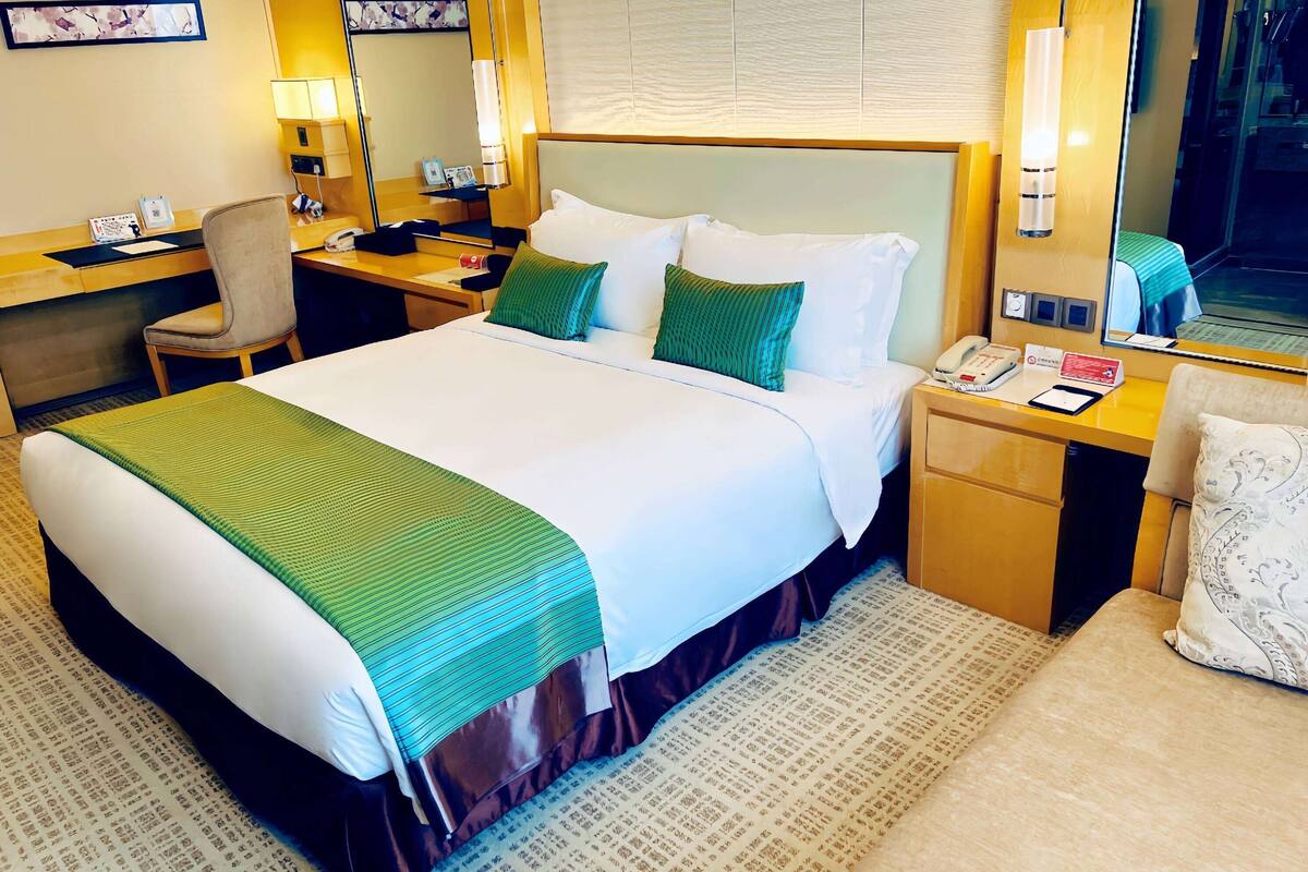Une chambre d’hôtel avec un grand lit, un bureau avec une chaise, une table de chevet avec une lampe et un miroir.