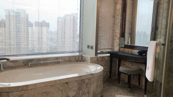 A modern bathroom with a large bathtub, a vanity with a mirror, and a city view through the windows.