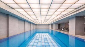Una piscina con suelo y paredes de azulejos, techo con diseño de cuadrícula y zona de estar con sillas y una mesa.