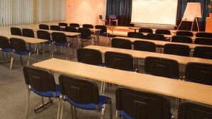 Ein Konferenzraum mit Reihen von Tischen und Stühlen, einer Projektionsleinwand und einer Bühne mit Rednerpult.