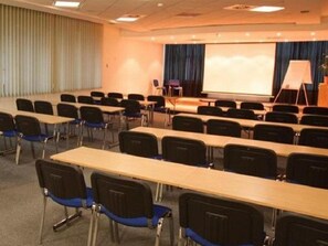 Ein Konferenzraum mit Reihen von Tischen und Stühlen, einer Projektionsleinwand und einer Bühne mit Rednerpult.