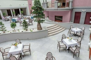 Une cour d’hôtel avec des sièges en plein air, un arbre au centre et un escalier menant à un niveau supérieur.