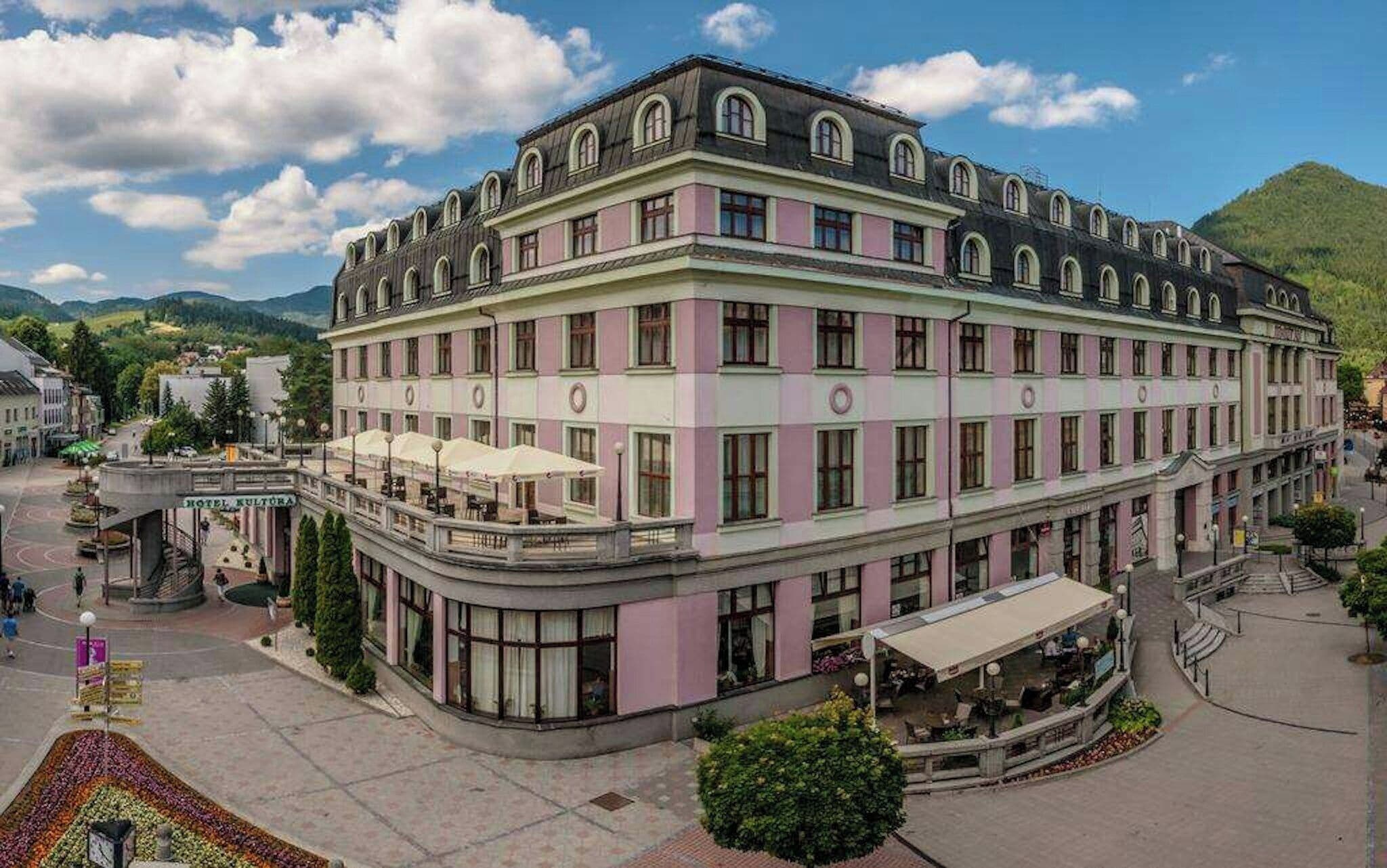 A multi-story hotel with a pink facade, a balcony with outdoor seating, and a central courtyard.