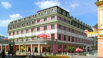 A multi-story hotel with a pink and white facade, outdoor seating with umbrellas, and a visible restaurant sign.