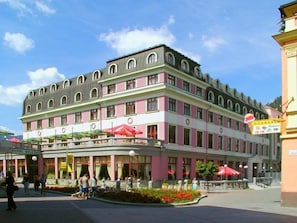 Ein mehrstöckiges Hotel mit rosafarben-weißer Fassade, Außenbereich mit Sonnenschirmen und einem sichtbaren Restaurantschild.