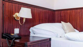 A hotel room with a wooden headboard, a bedside lamp, a telephone, and a bed with white bedding.
