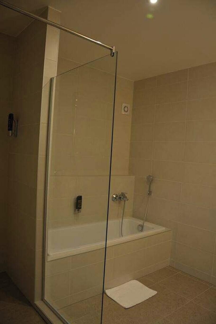 Un espace douche clos par des parois de verre, comprenant une baignoire, une douchette à main et un panneau de commande.