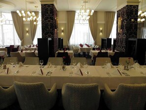 Un espace repas avec des tables dressées, des lustres et un papier peint à motifs.