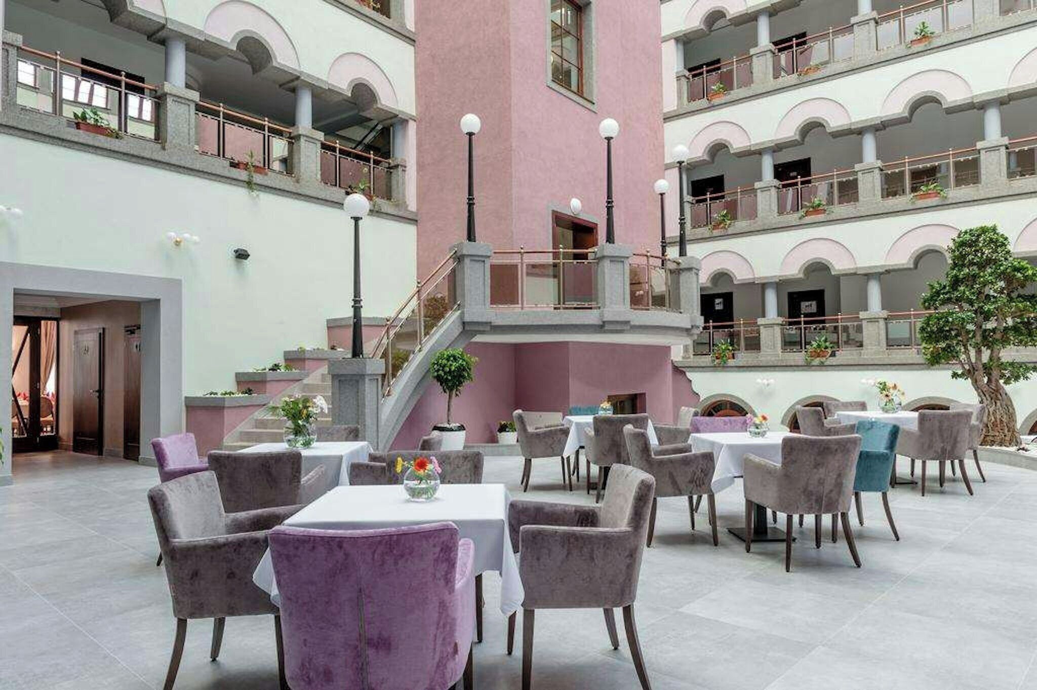 A multi-level atrium with a central staircase, multiple seating areas with tables and chairs, and balconies on each floor.