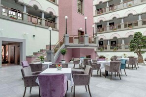 Ein mehrgeschossiges Atrium mit einer zentralen Treppe, mehreren Sitzbereichen mit Tischen und Stühlen sowie Balkonen in jeder Etage.