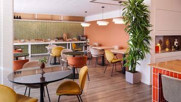 A modern cafe interior with round tables, chairs, and a kitchen area in the background.