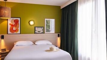 A hotel room with a large bed, a headboard, wall-mounted artwork, a bedside lamp, and a window with curtains.