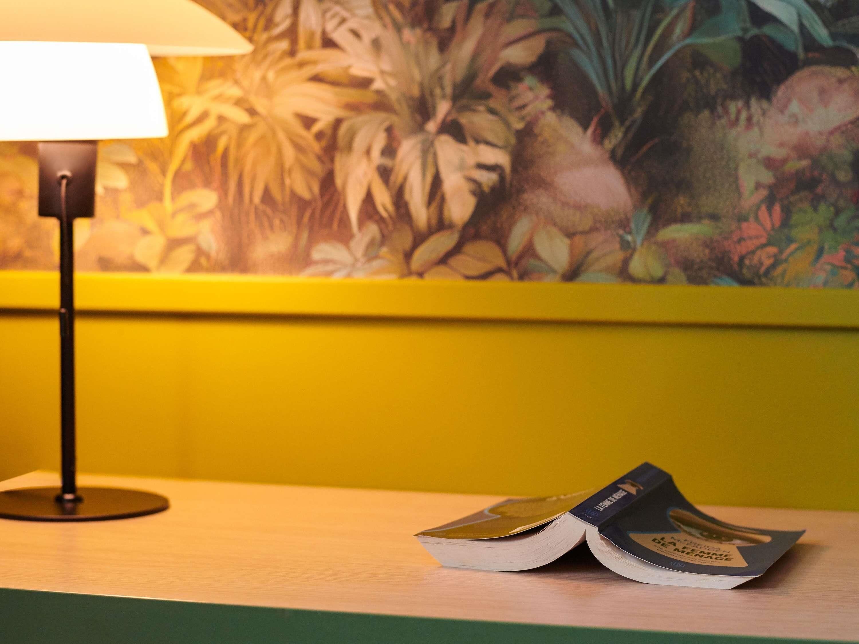 Un libro sobre una superficie de madera con una lámpara y una pared con estampado floral.