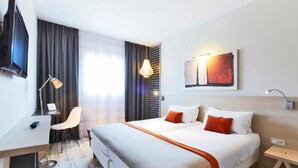 A modern hotel room with a large bed, a desk with a chair, a flat-screen TV, and a painting on the wall. - ibis Styles Vannes Porte du Golfe (Vannes)