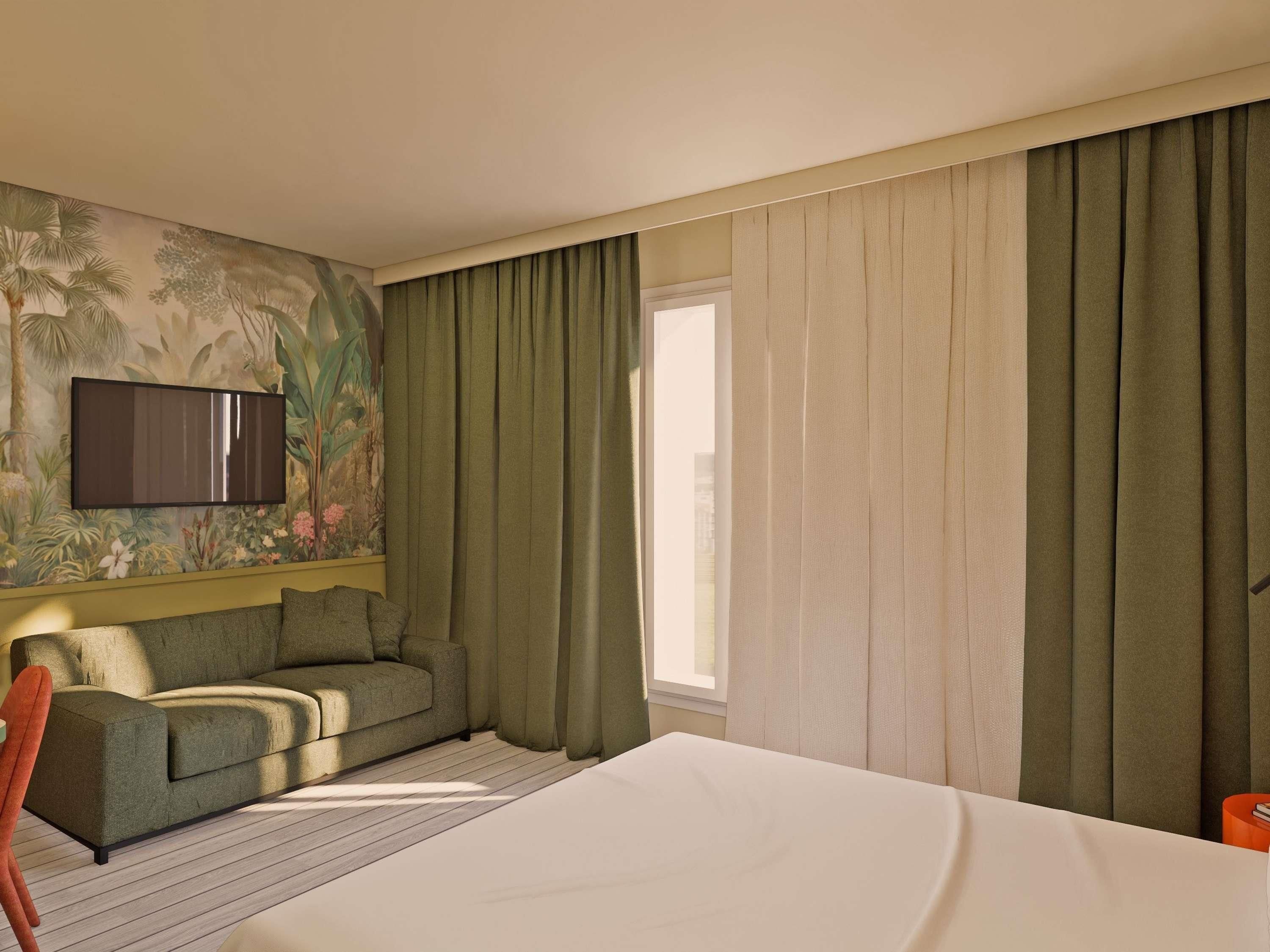A hotel room with a bed, a sofa, a TV mounted on the wall, and a window with curtains.