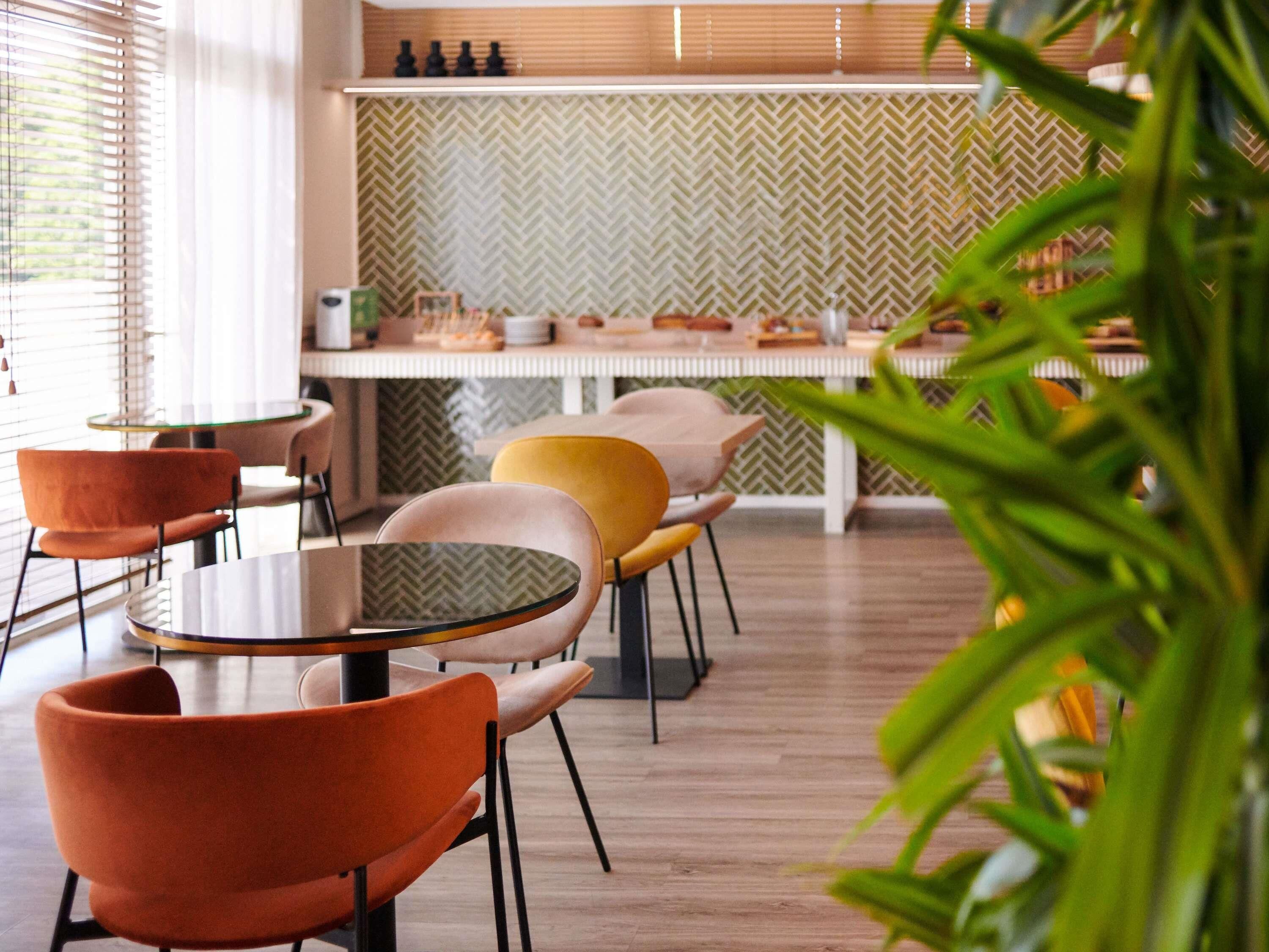 A modern dining area with round tables and chairs, a herringbone-patterned wall, and a wooden floor.