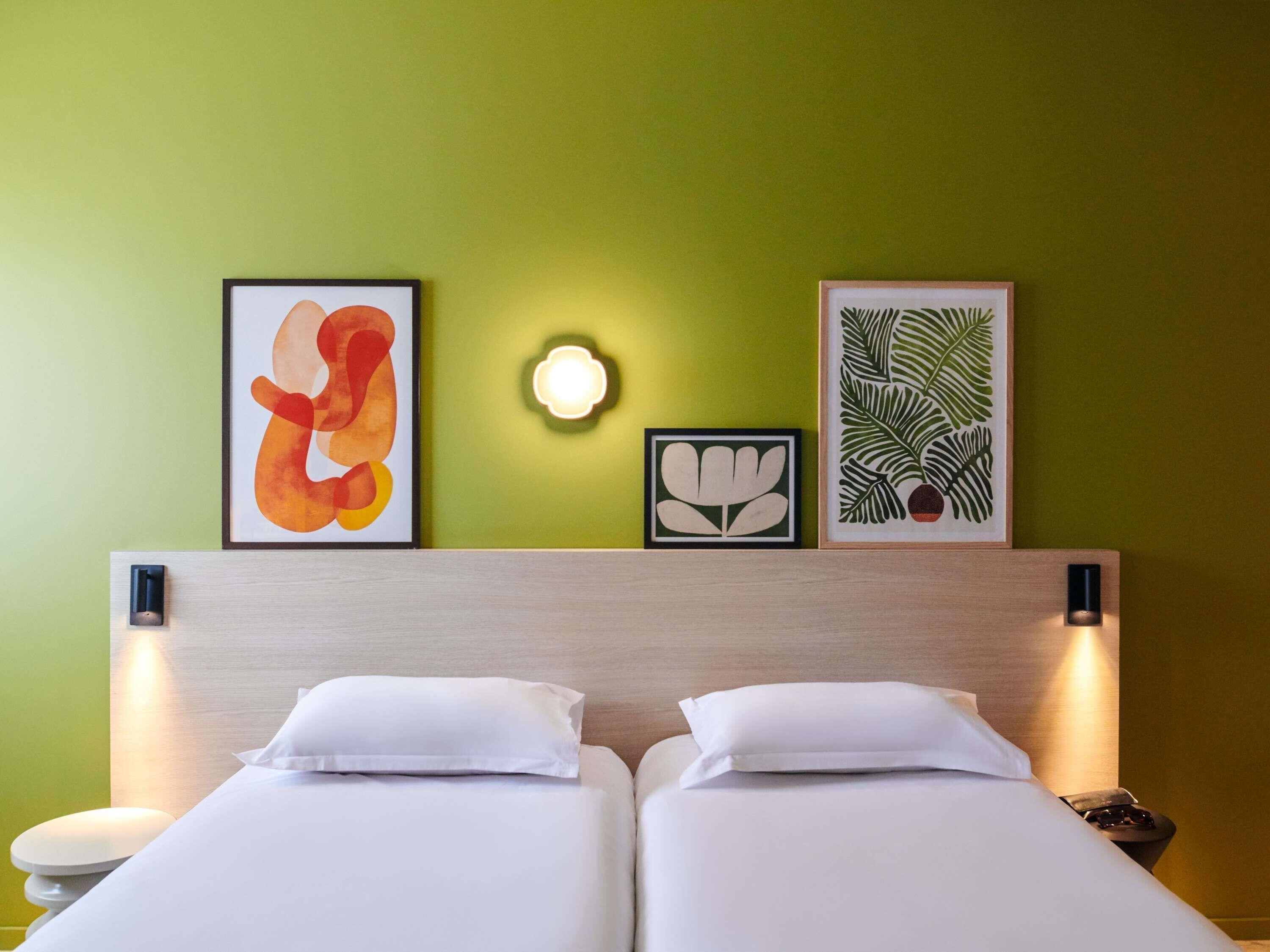 Una habitación de hotel con una cama, dos almohadas, una mesita de noche y tres cuadros enmarcados en la pared.