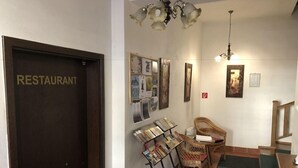 Un espace d’accueil avec une enseigne « RESTAURANT », un mur décoré de photos, des chaises en osier, une petite table et un escalier.