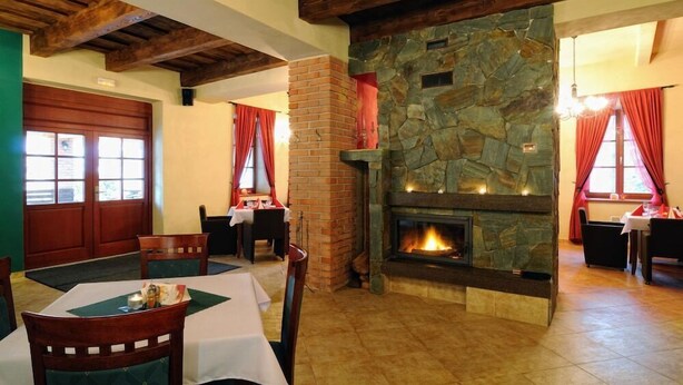 Un coin repas agrémenté d’une cheminée en pierre, de poutres en bois et de rideaux rouges.