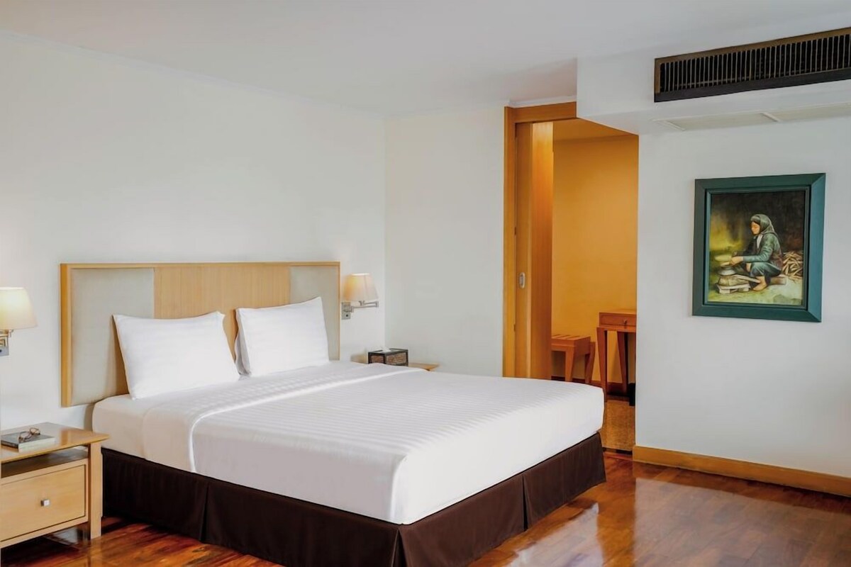 A hotel room with a large bed, bedside tables, a painting on the wall, and a wooden floor.