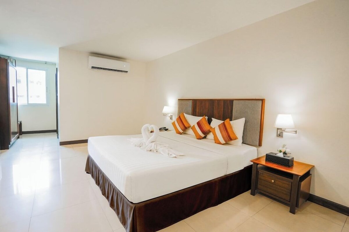Ein Hotelzimmer mit einem großen Bett, zwei Nachttischlampen, einem Nachttisch und einer Klimaanlage.