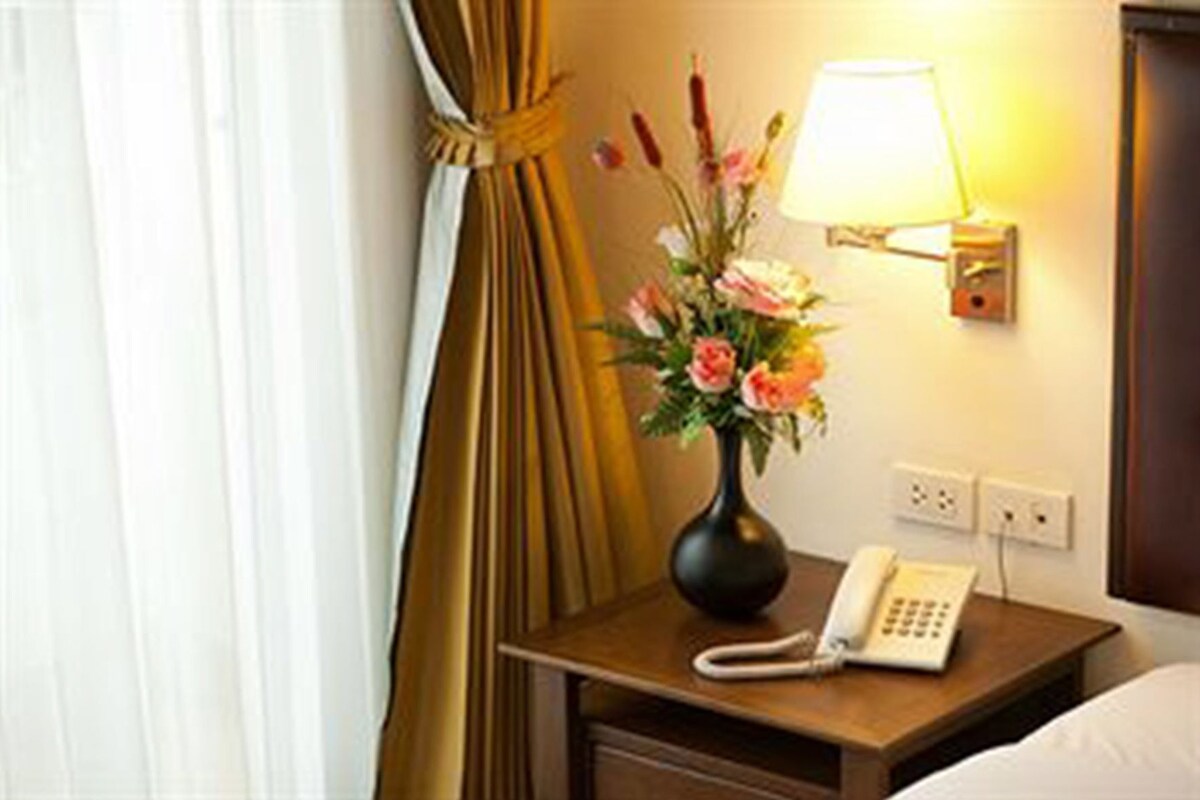 Ein Hotelzimmer mit Nachttisch, Lampe, Blumen in einer Vase, Telefon und Bett.