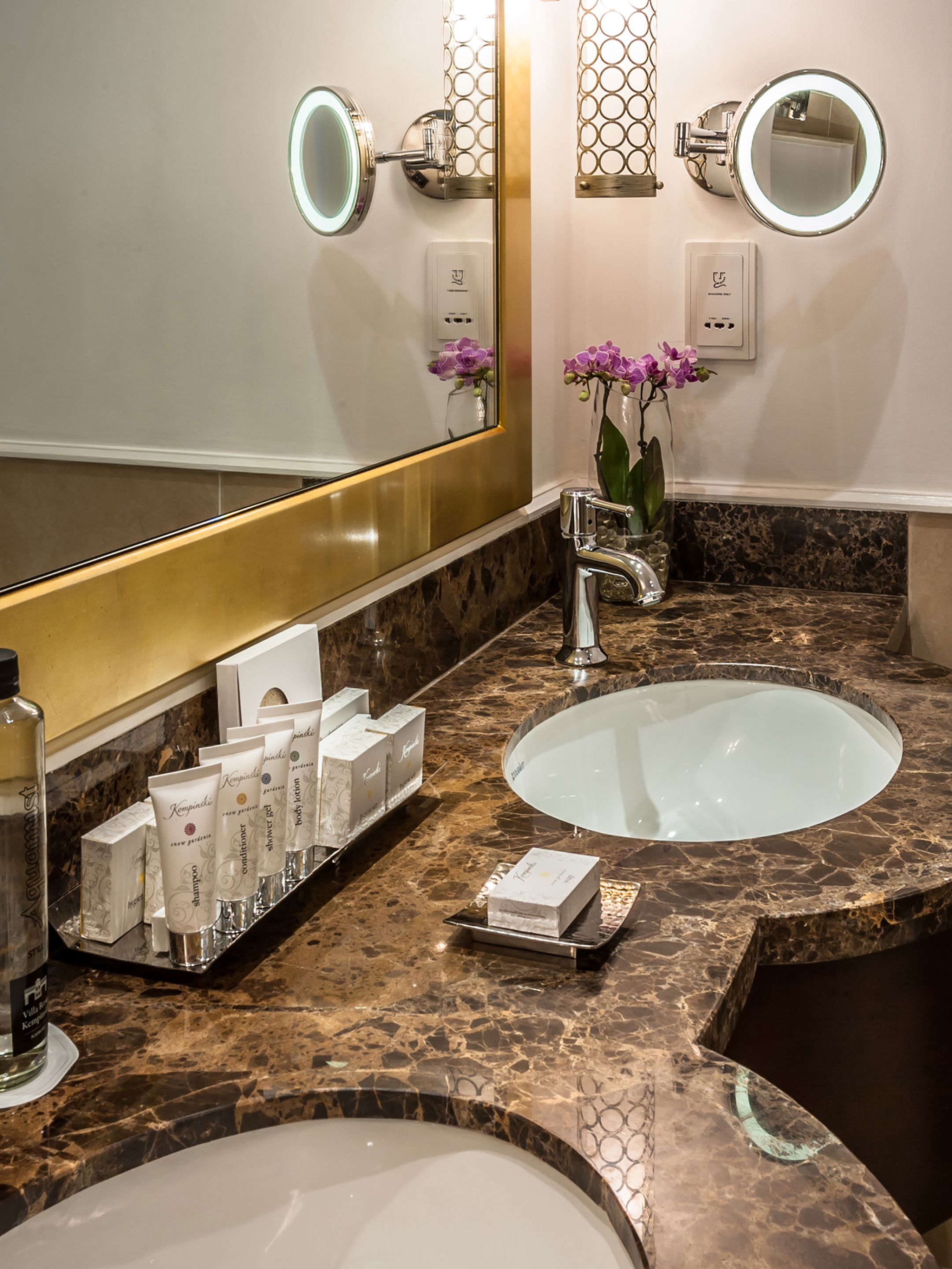 Un baño con dos lavamanos, un espejo grande y una zona de tocador con artículos de aseo.