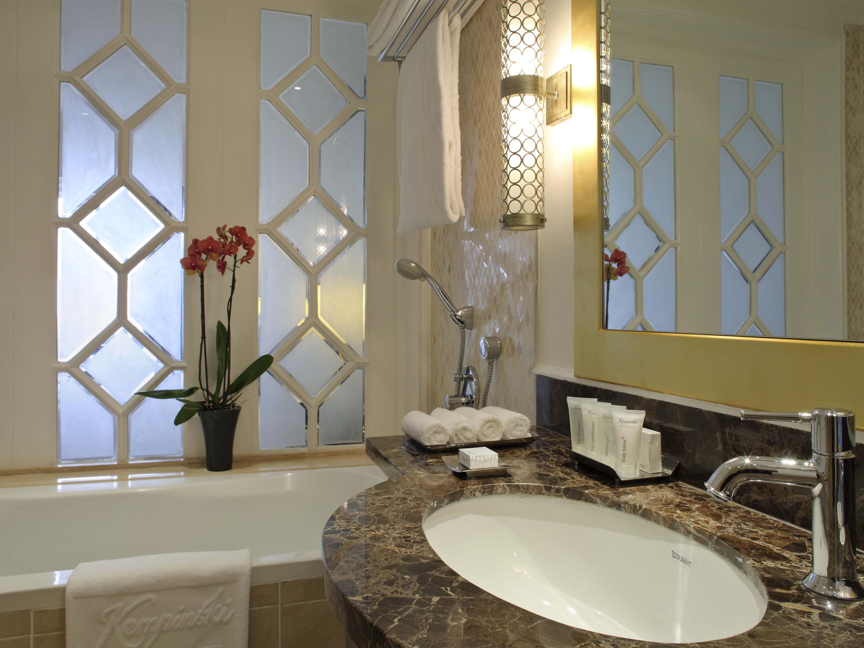 A bathroom with a large bathtub, a marble sink, a mirror, and a potted orchid.