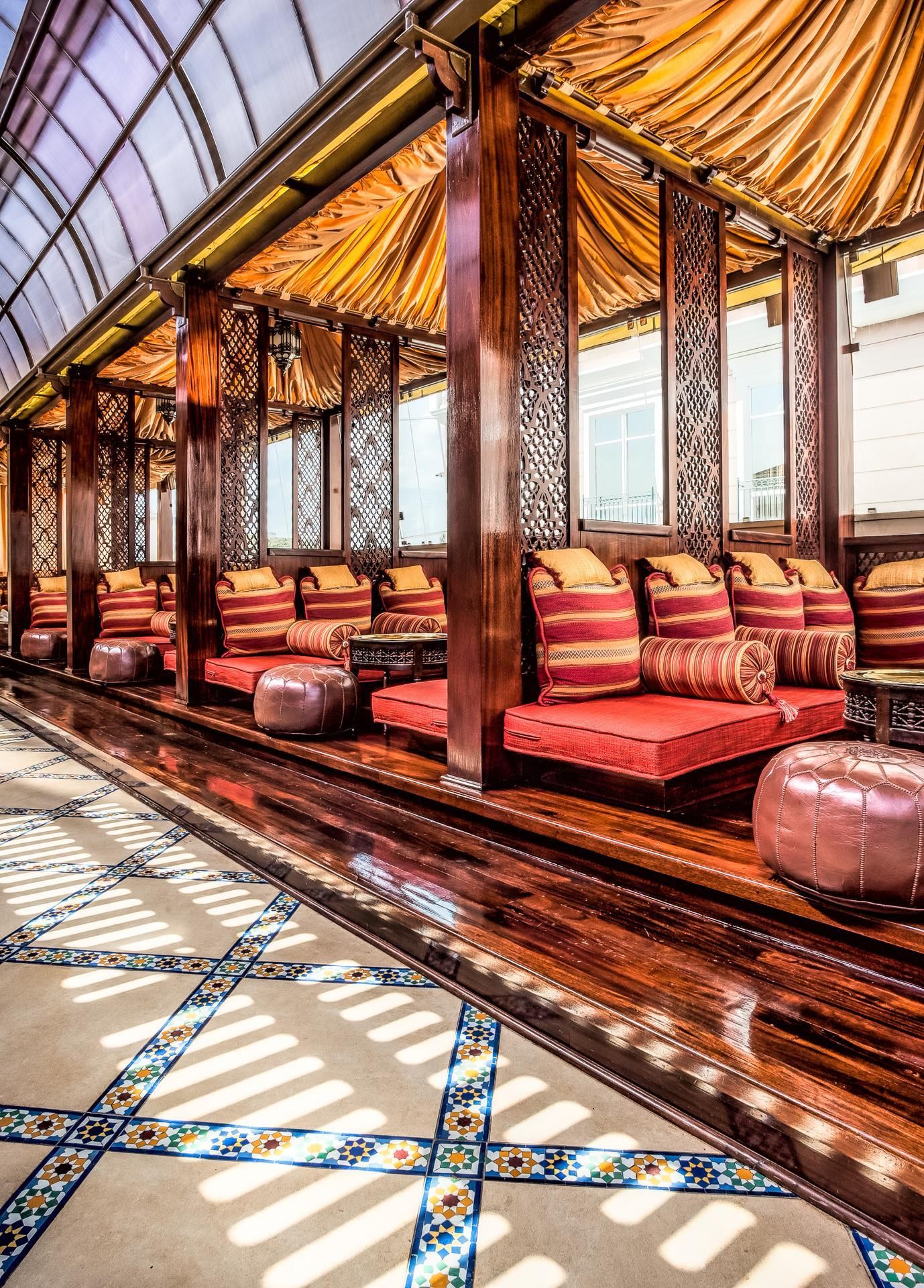 A row of wooden benches with cushions, a patterned floor, and a high ceiling with a translucent roof.