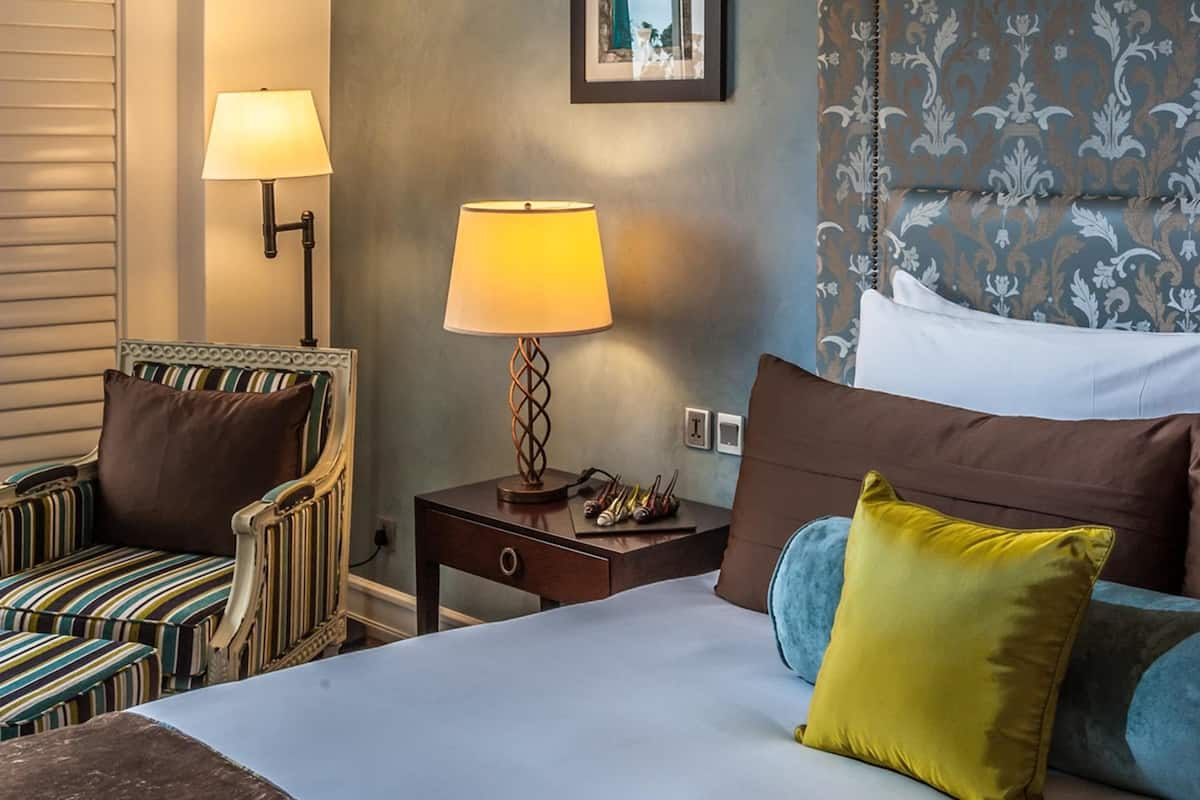 A hotel room with a bed, two bedside lamps, a chair, a nightstand, and a mirror on the wall.