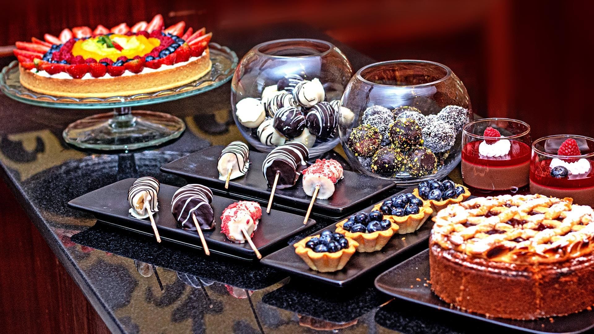 A variety of desserts on a buffet table, including a cake with fruit, chocolate-covered treats, and small tarts.