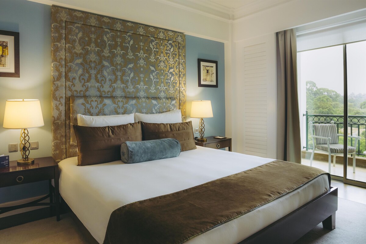 A hotel room with a large bed, two bedside tables, a nightstand, a window with a view, and a balcony.