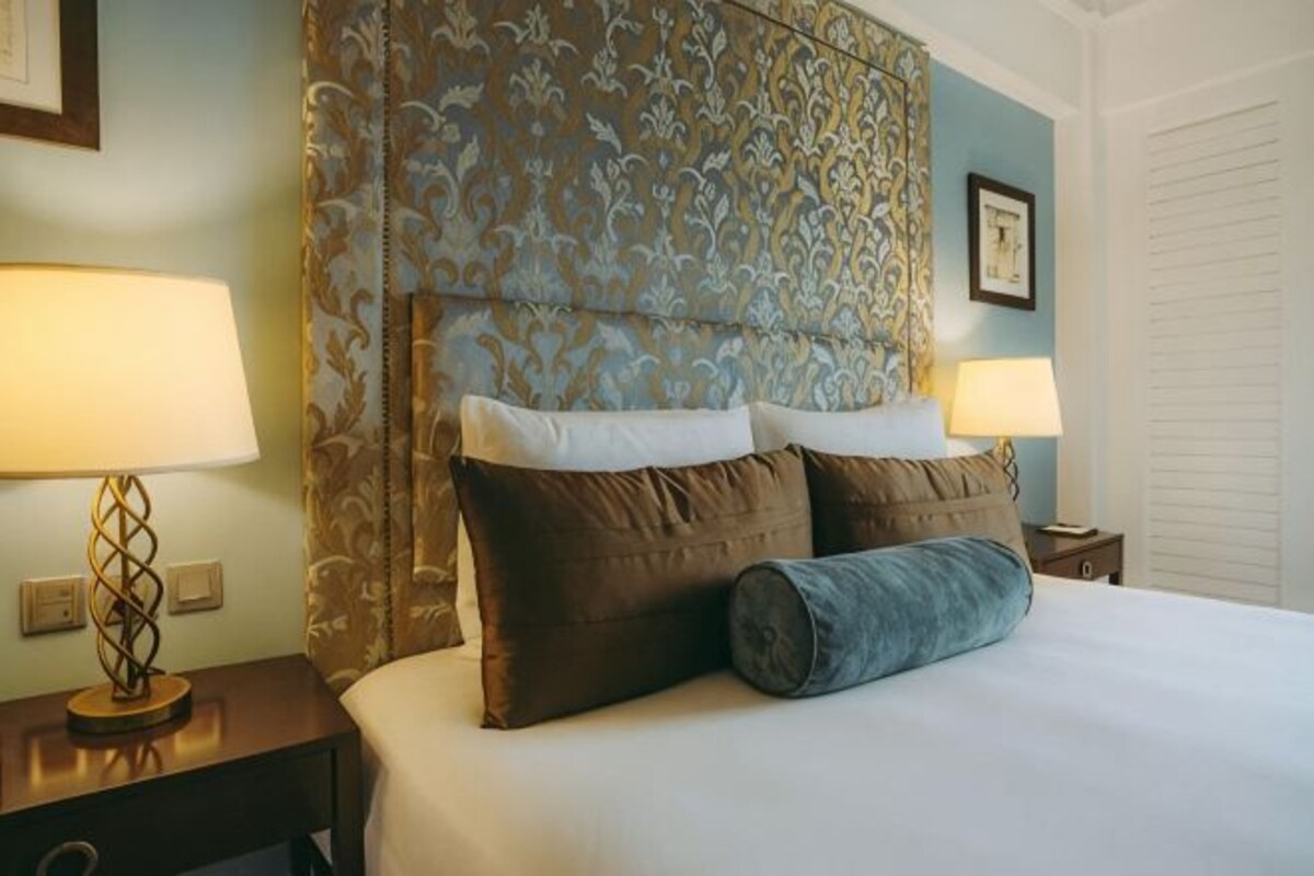 A hotel room with a large bed, two bedside tables, a patterned headboard, and two wall-mounted lamps.