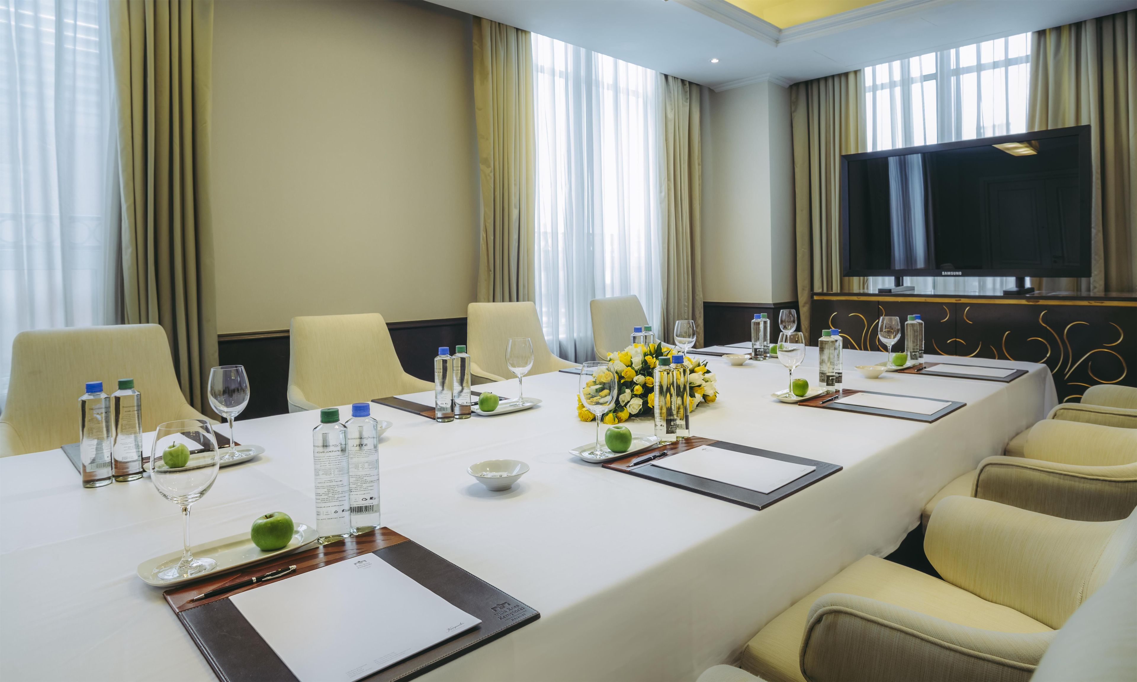 A conference room with a long table, chairs, water bottles, glasses, a bouquet of flowers, and a television.