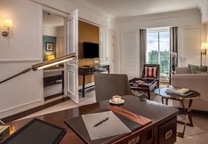 A hotel room with a desk, a chair, a sofa, a TV, and a balcony with a view.