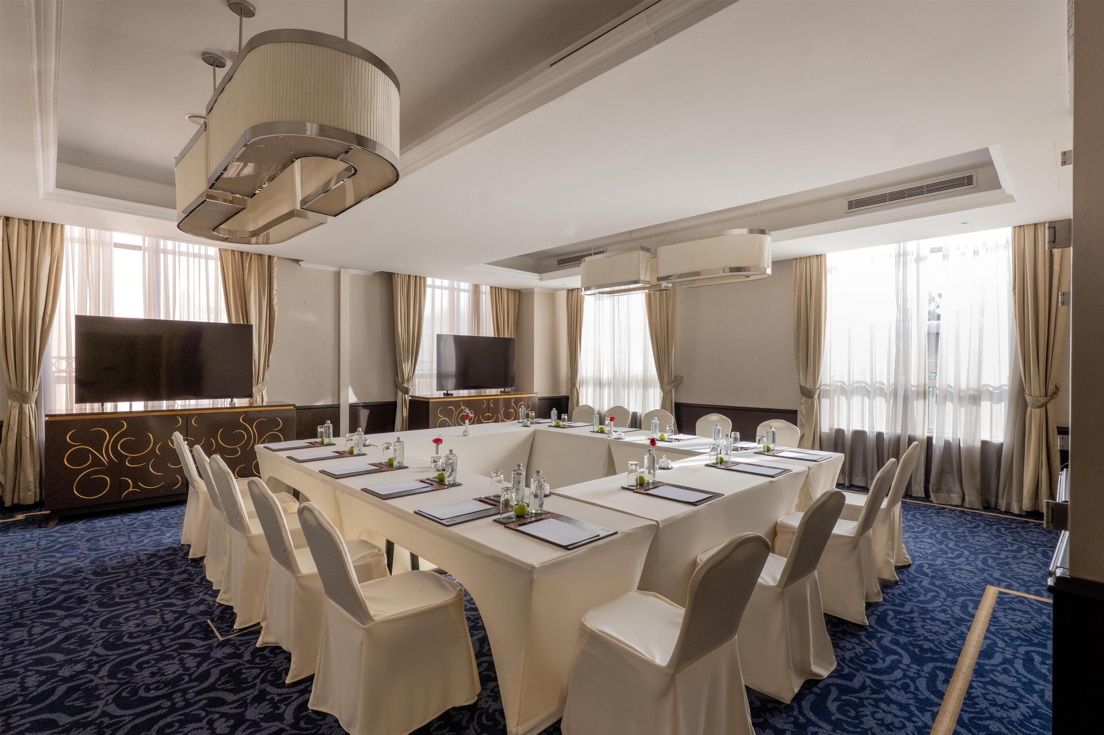 Ein Konferenzraum mit einem langen Tisch, Stühlen, einem Fernseher und einer dekorativen Deckenleuchte.