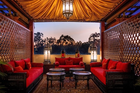 A cozy lounge area with red sofas, small round tables, and decorative lanterns.