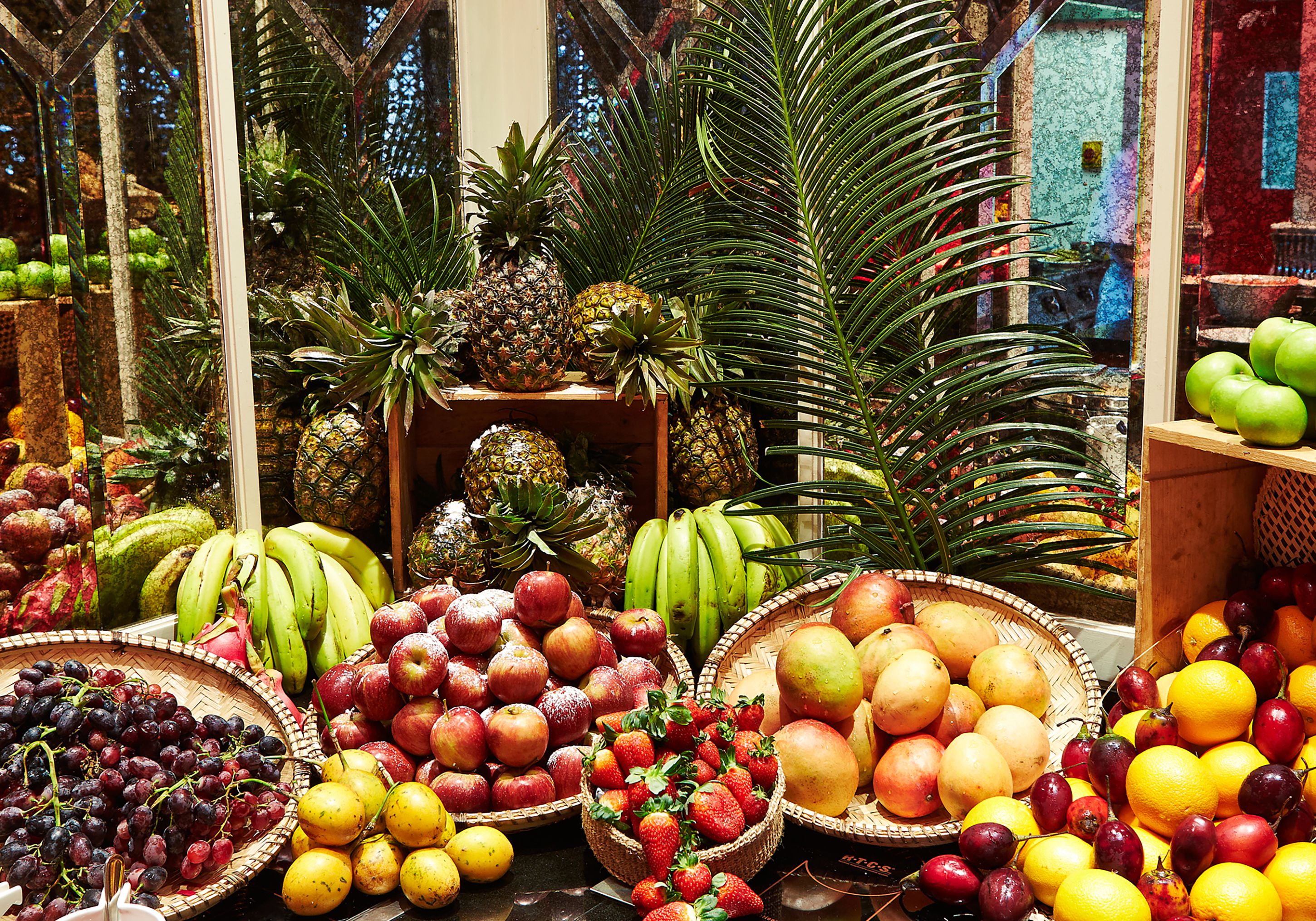 A fruit stand with various fruits and a tropical plant in the background.