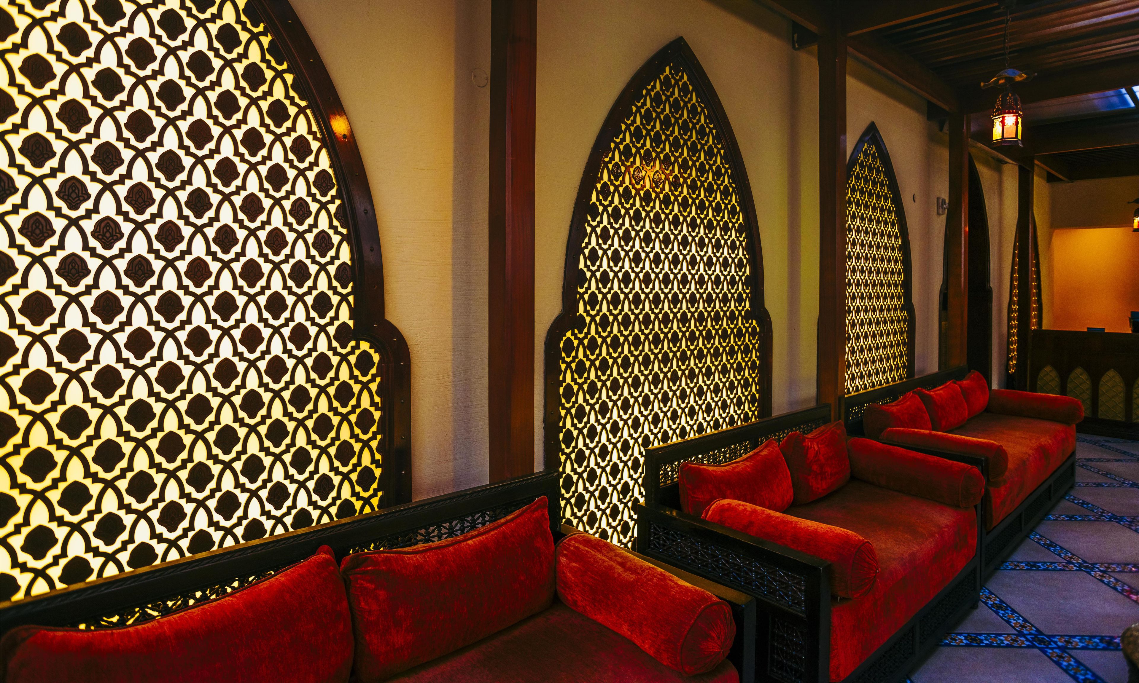 A room with a row of red upholstered sofas, a patterned wall, and a patterned window.