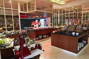 A buffet area with a central island, various food stations, and a large window providing a view of the outside.