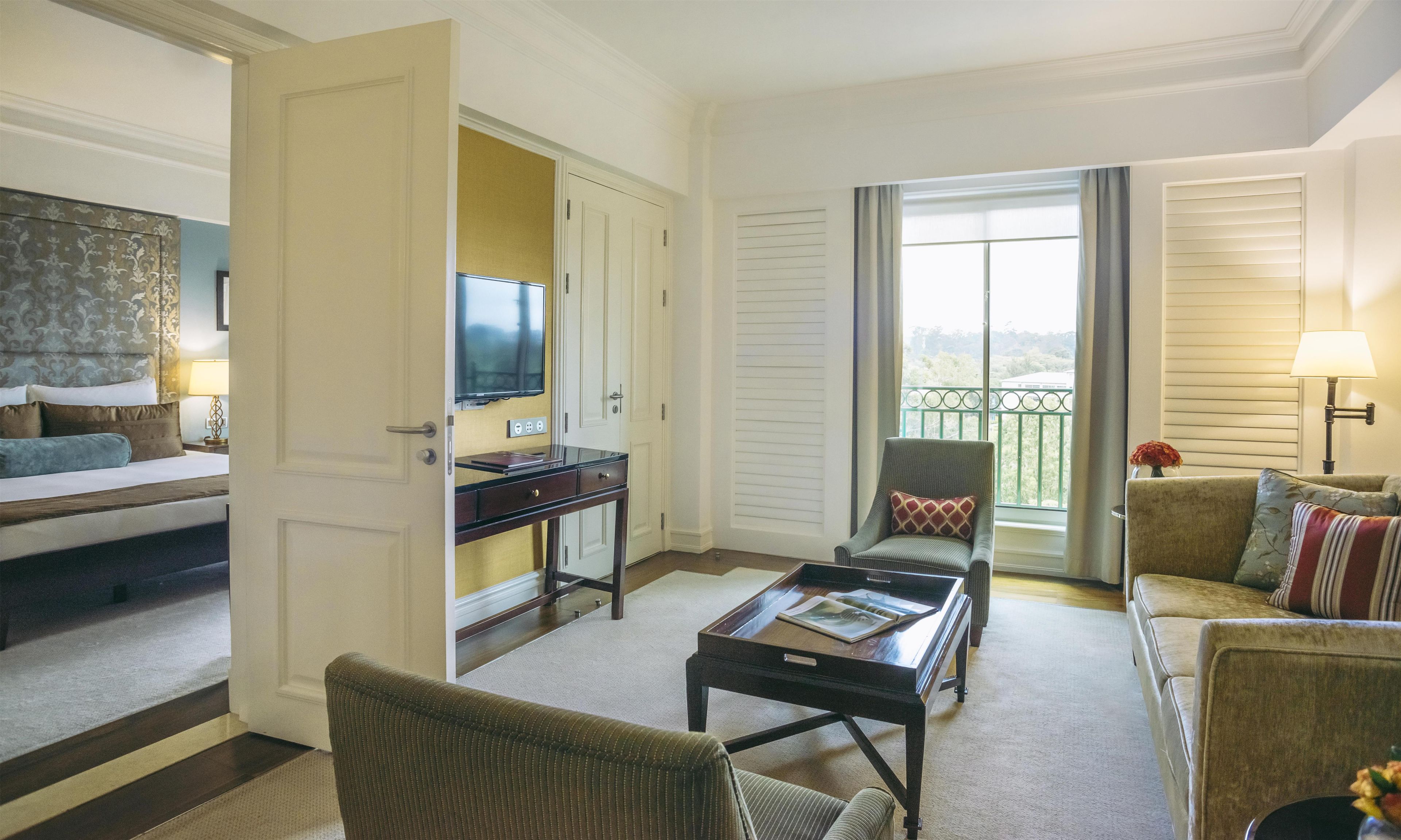 A hotel room with a bed, a desk with a TV, a balcony with a view, and a sofa.