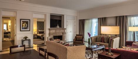 A hotel room with a dining table, chairs, a sofa, a fireplace, and a TV.