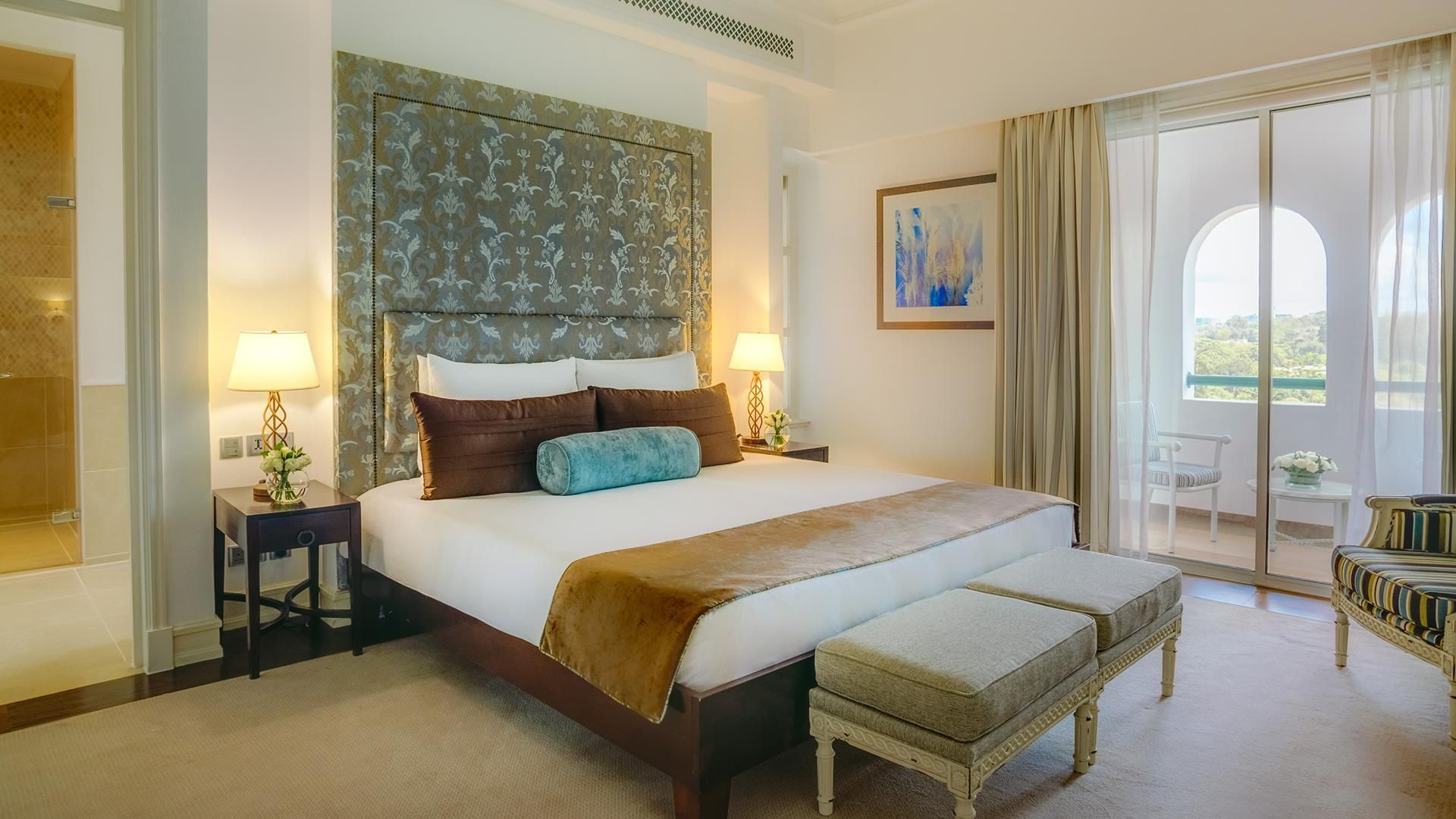 A hotel room with a large bed, a sitting area, and a balcony with a view.